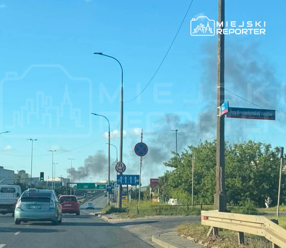 Na drodze widoczne samochody, w tle unoszący się dym nad miastem, znak uliczny "Przy Bernardyńskiej Wodzie".