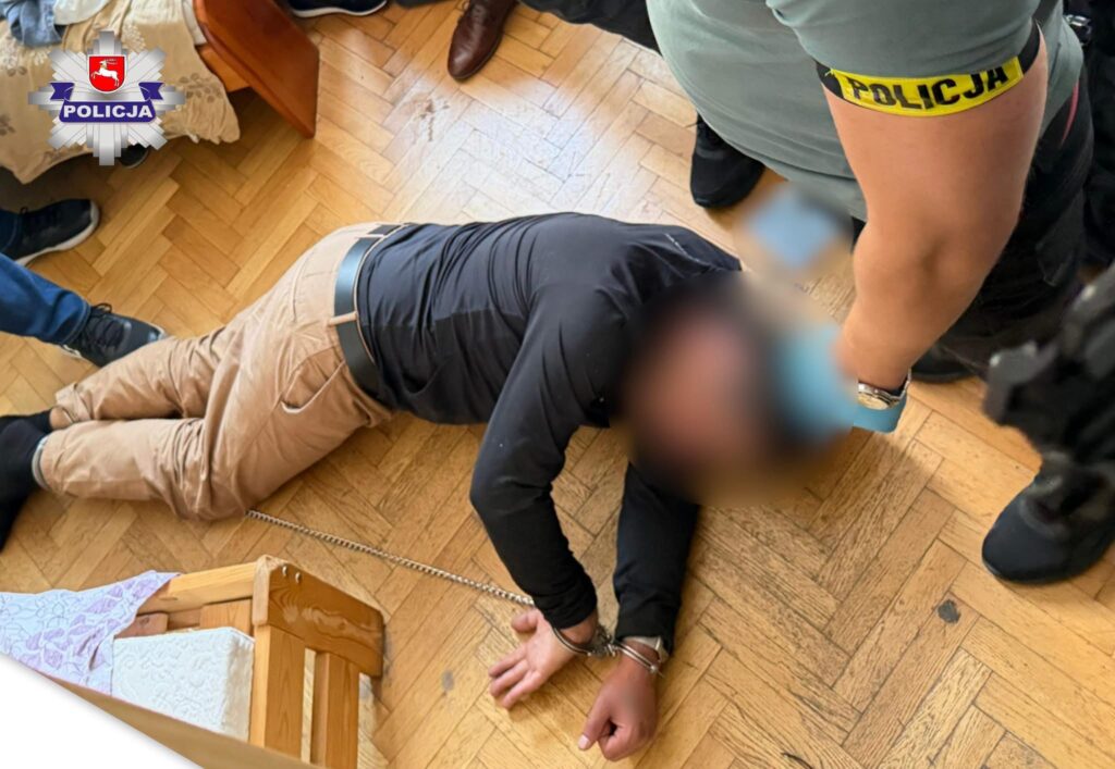 Mężczyzna leży na podłodze w pomieszczeniu, z rękami skuty kajdankami, otoczony przez funkcjonariuszy policji.