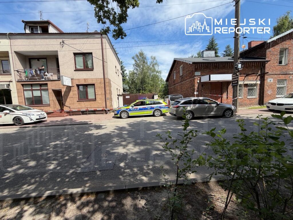 Policjant w mundurze rozmawia z kierowcą przy radiowozie na ulicy obok budynku mieszkalnego.