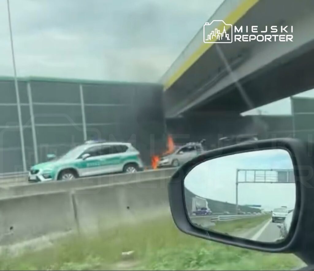 Samochód zapalił się na autostradzie, obok widoczny radiowóz oraz dym unoszący się pod mostem.