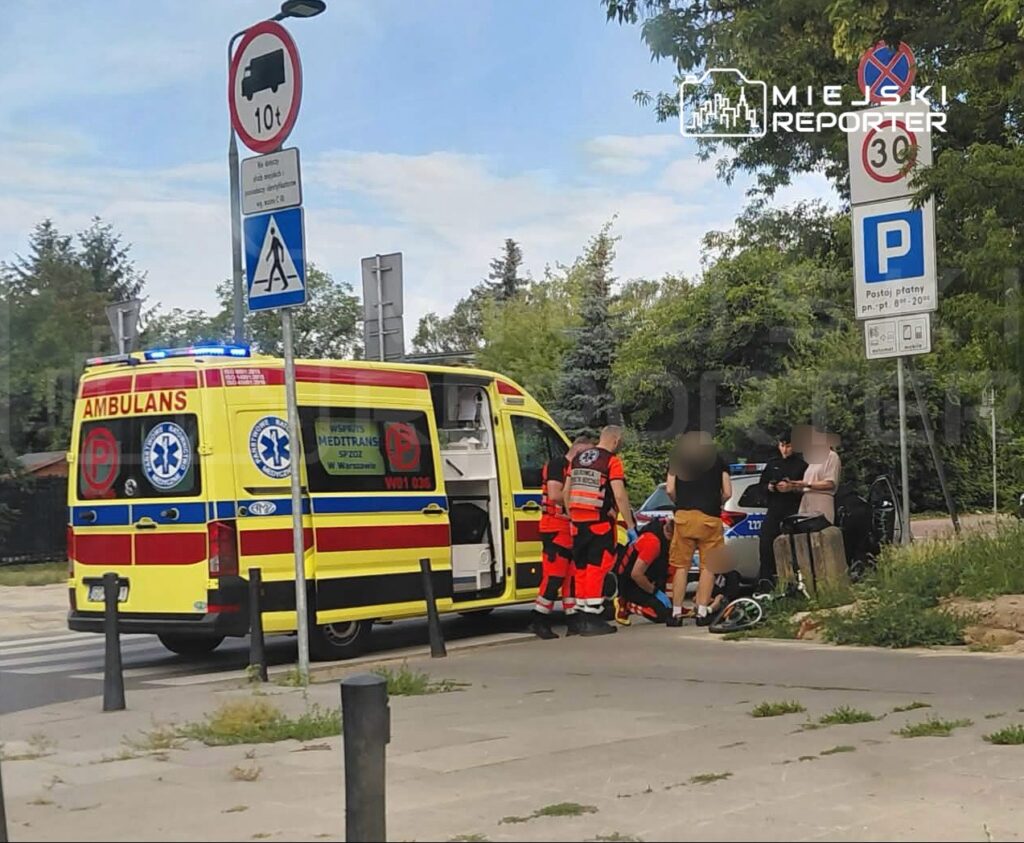 Zespół ratowników medycznych udziela pomocy poszkodowanemu na chodniku obok karetki w mieście.