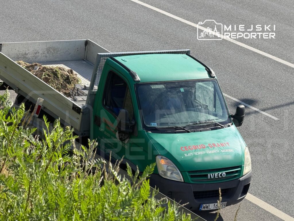 Zielony samochód dostawczy z ładunkiem ziemi zatrzymany na drodze, w otoczeniu zieleni.