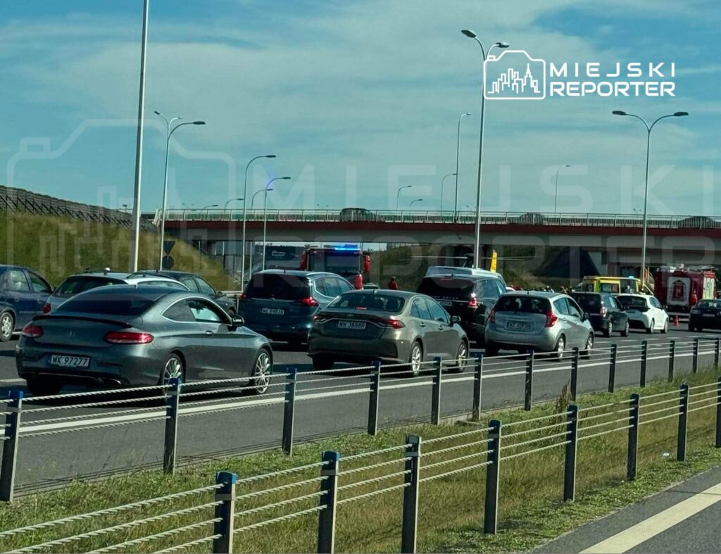 Zator drogowy na autostradzie, w tle widać pojazdy ratunkowe oraz most z oświetleniem.