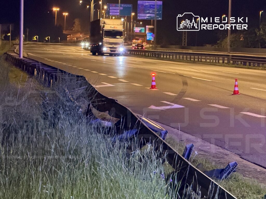 Na drodze ekspresowej w nocy widoczny jest uszkodzony barierka ochronna oraz oznakowanie w postaci pachołków.
