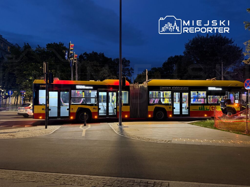 Jedenastka elektryczny autobus zatrzymuje się na skrzyżowaniu, w tle widoczne są światła drogowe i zieleń.