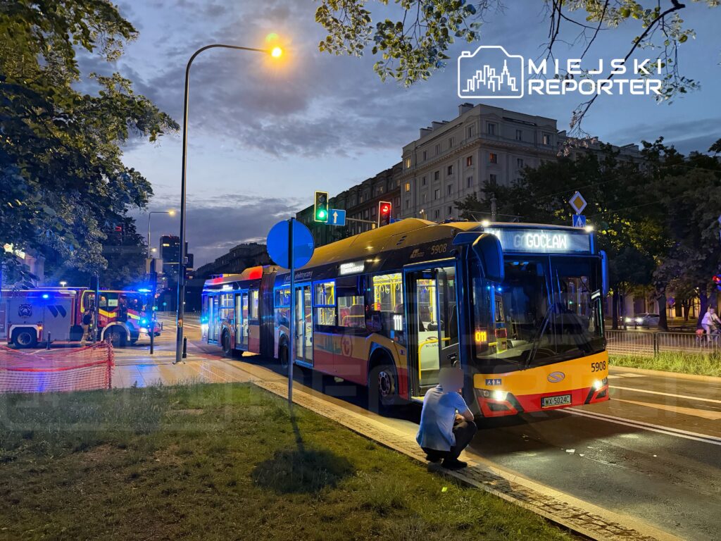 Autobus miejski zatrzymany na przystanku, w tle widać woz strażacki z włączonymi sygnałami świetlnymi.