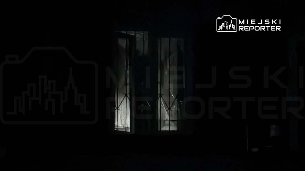 Oświetlone okno z zasłonami w ciemnym otoczeniu nocnym.