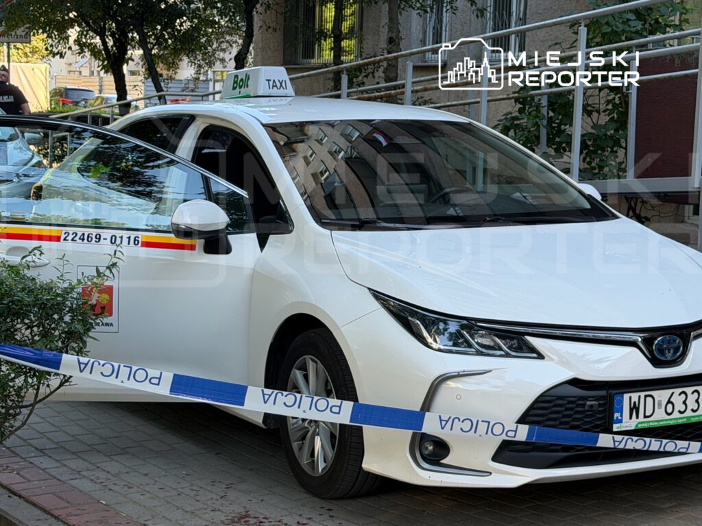 Białe auto taxi z napisem "Bolt" zatrzymane przy chodniku, otwarte drzwi, obok niebieska taśma policyjna.