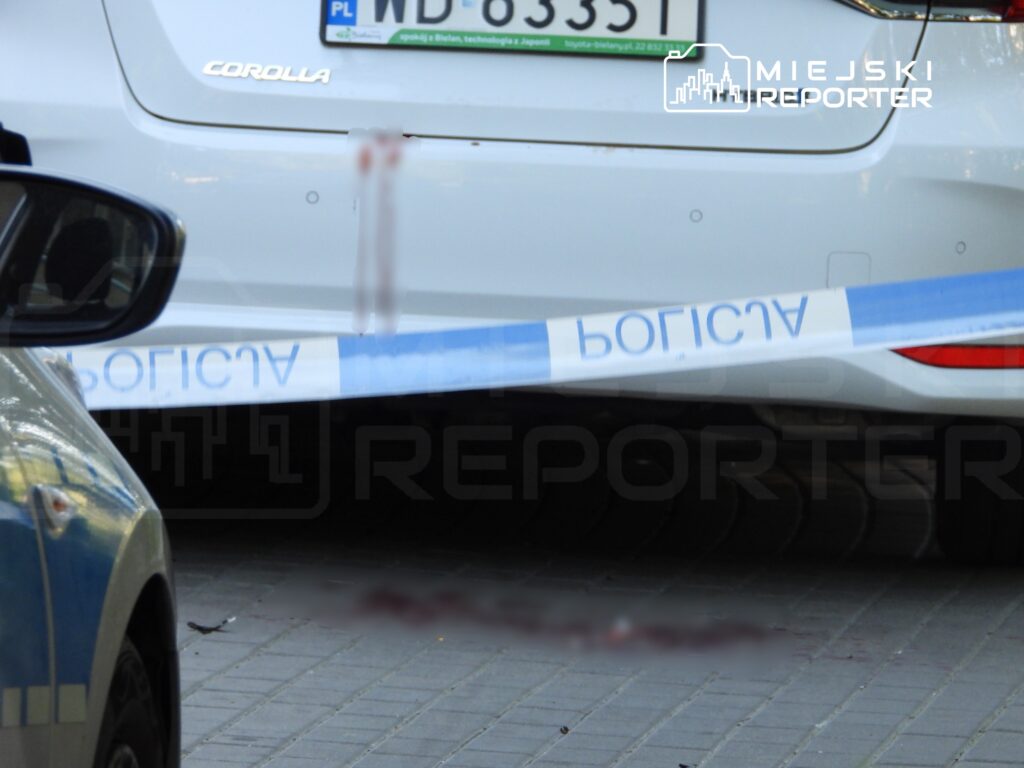 Samochód osobowy z widocznym uszkodzeniem tyłu, otoczony taśmą policyjną na chodniku.