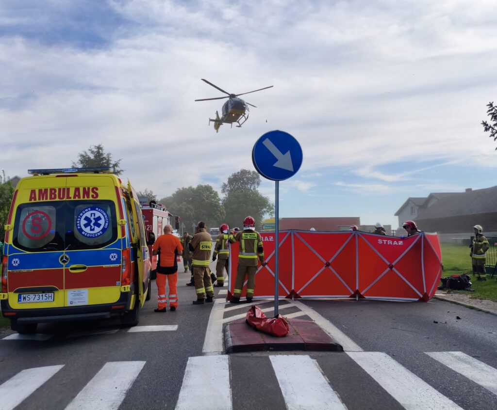 Zespół ratunkowy w akcji przy drodze, z helikopterem nad głowami i ustawioną osłoną ochronną.