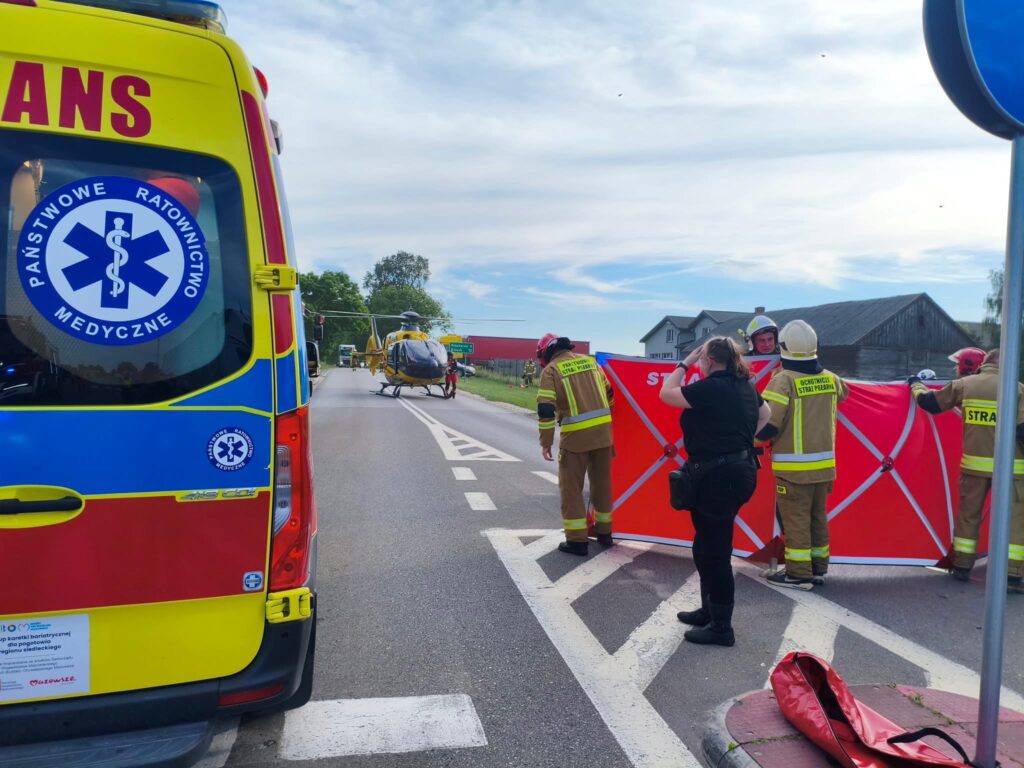 Zespół ratunkowy ustawia czerwony parawan na drodze, podczas lądowania helikoptera ratunkowego.