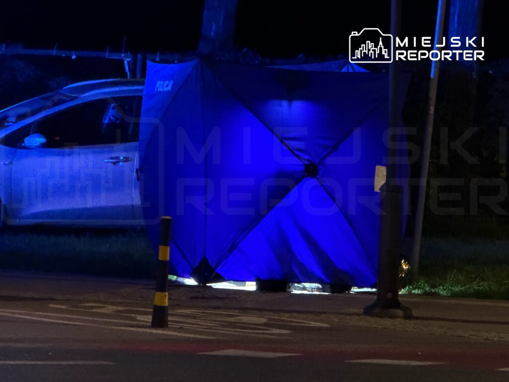 Policja zabezpiecza miejsce zdarzenia pod niebieską namiotem w pobliżu zaparkowanego samochodu.
