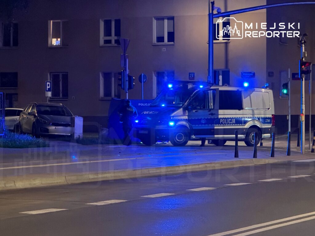 Policjant przy policyjnym samochodzie z włączonymi sygnałami niebieskimi na ulicy w nocy.