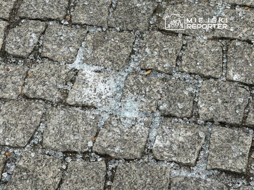 Szkło rozbite na kostce brukowej, tworząc niebezpieczne fragmenty w otoczeniu.