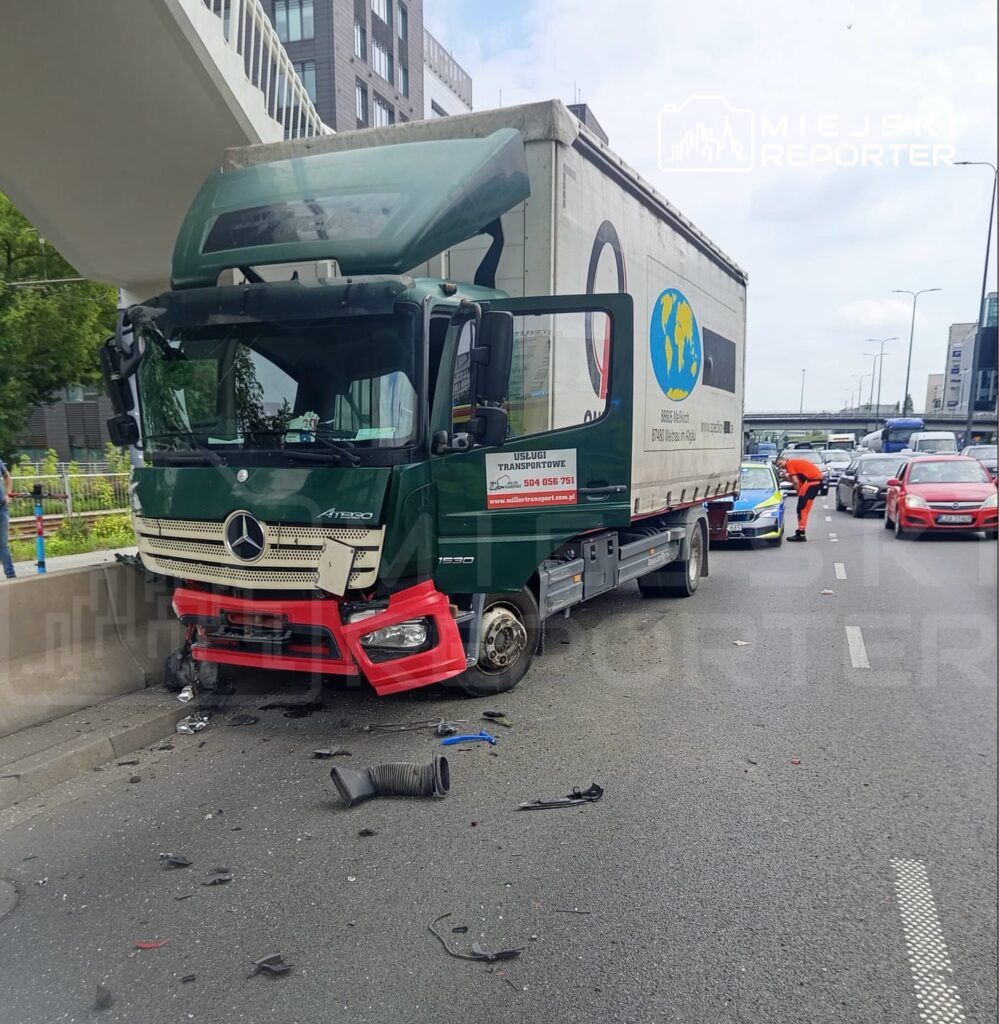 Zniszczona ciężarówka Mercedes z uszkodzoną przednią częścią stoi na drodze, obok leżą resztki części.