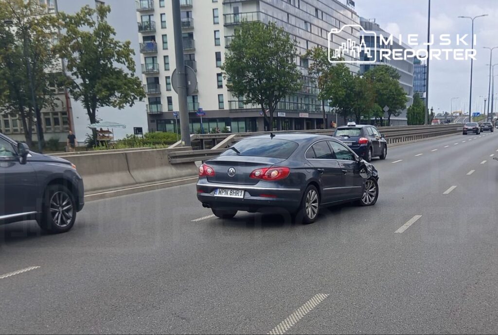 Uszkodzony samochód osobowy marki Volkswagen stojący na ruchliwej ulicy, obok innych pojazdów.