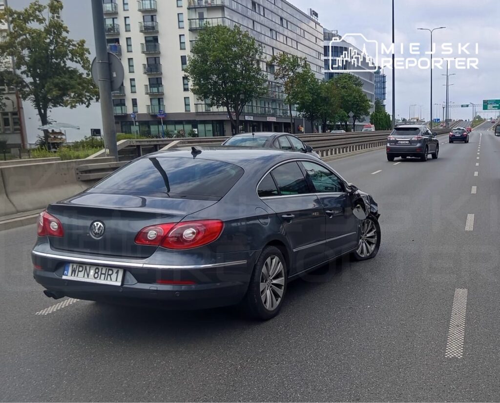 Uszkodzony samochód osobowy marki Volkswagen stoi na ruchliwej drodze, obok innych pojazdów.