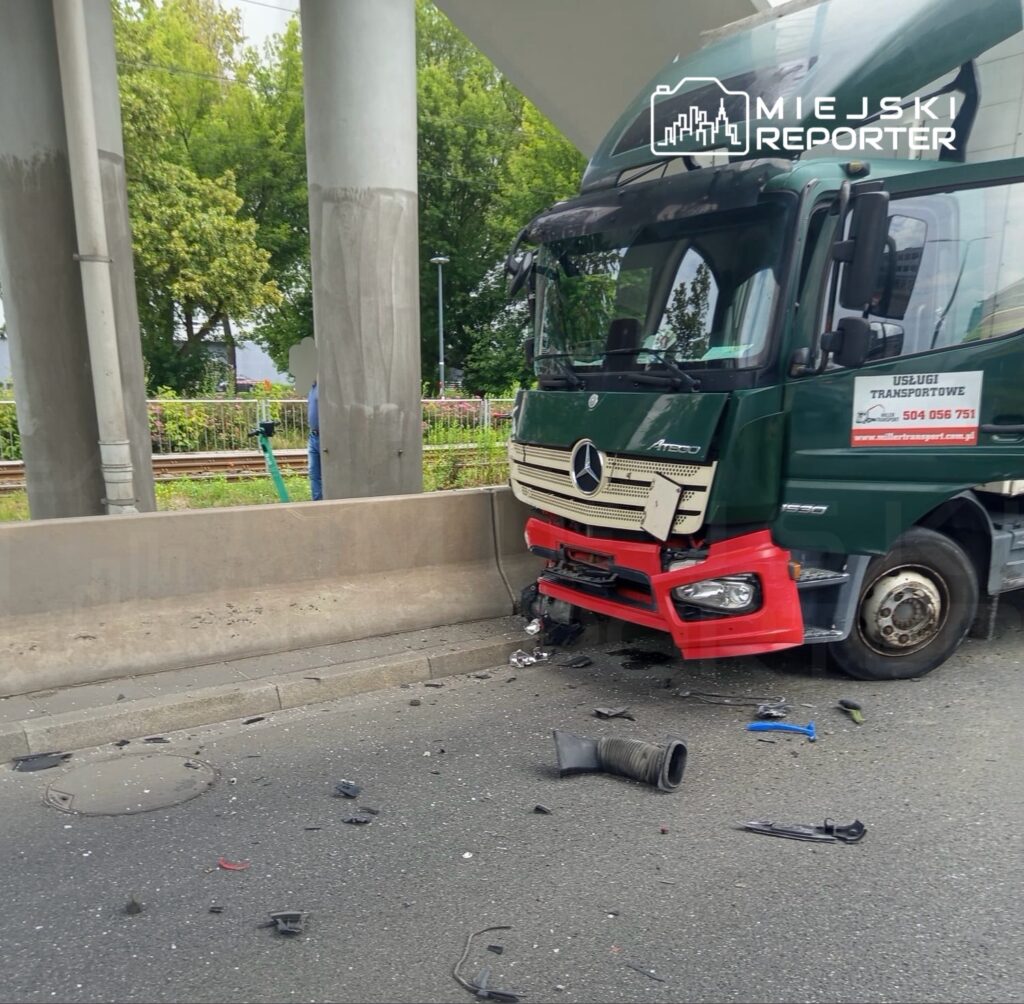 Zniszczona ciężarówka marki Mercedes z uszkodzoną przednią częścią stoi na jezdni, wokół leżą fragmenty pojazdu.