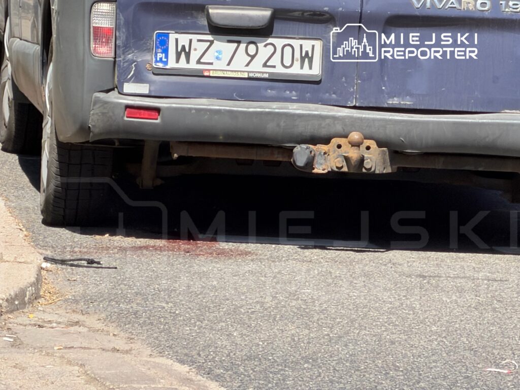 Samochód dostawczy zaparkowany na ulicy, z plamą krwi na nawierzchni obok tylnego koła.