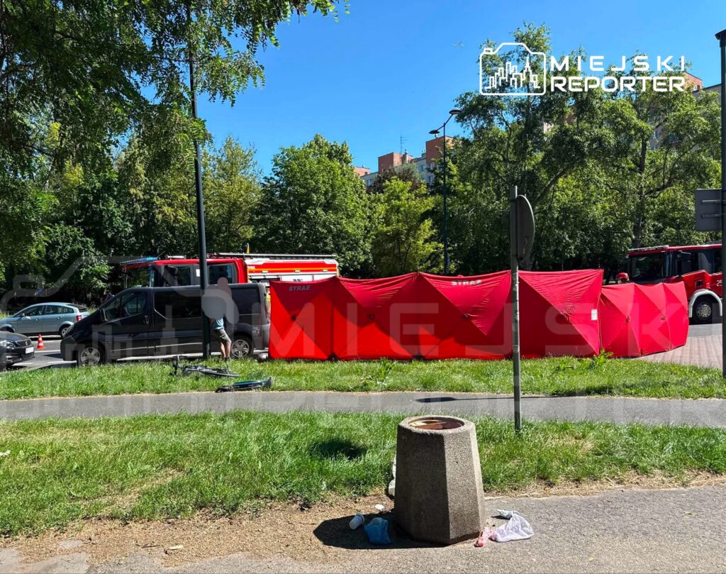 Czerwone namioty ratunkowe ustawione przy drodze, obok straży pożarnej oraz zaparkowanego samochodu.