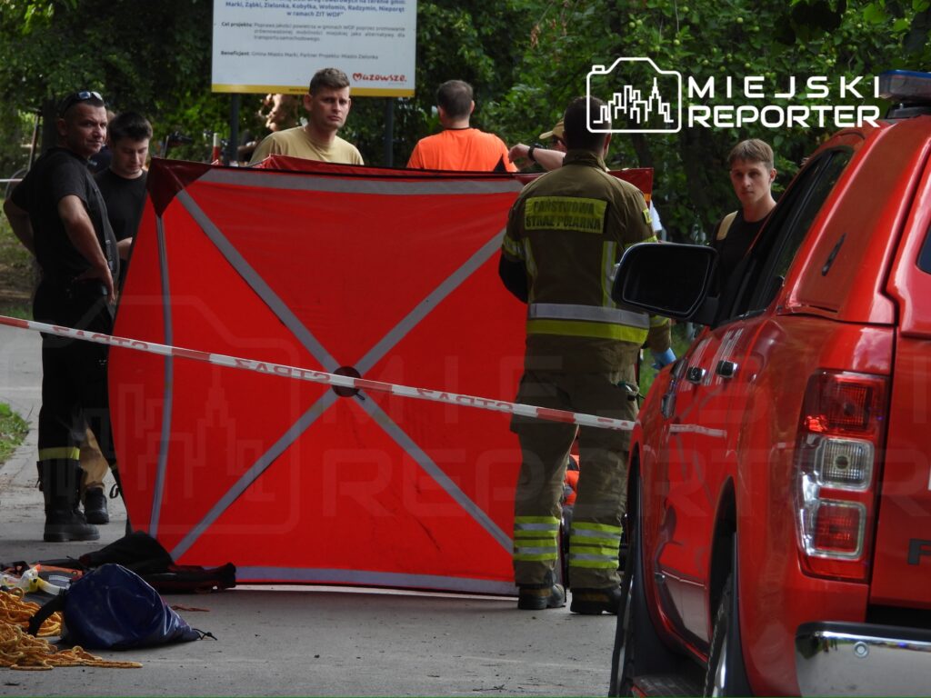 Grupa ratowników i strażaków pracuje przy czerwonym namiocie w terenie, zabezpieczonym taśmą ostrzegawczą.