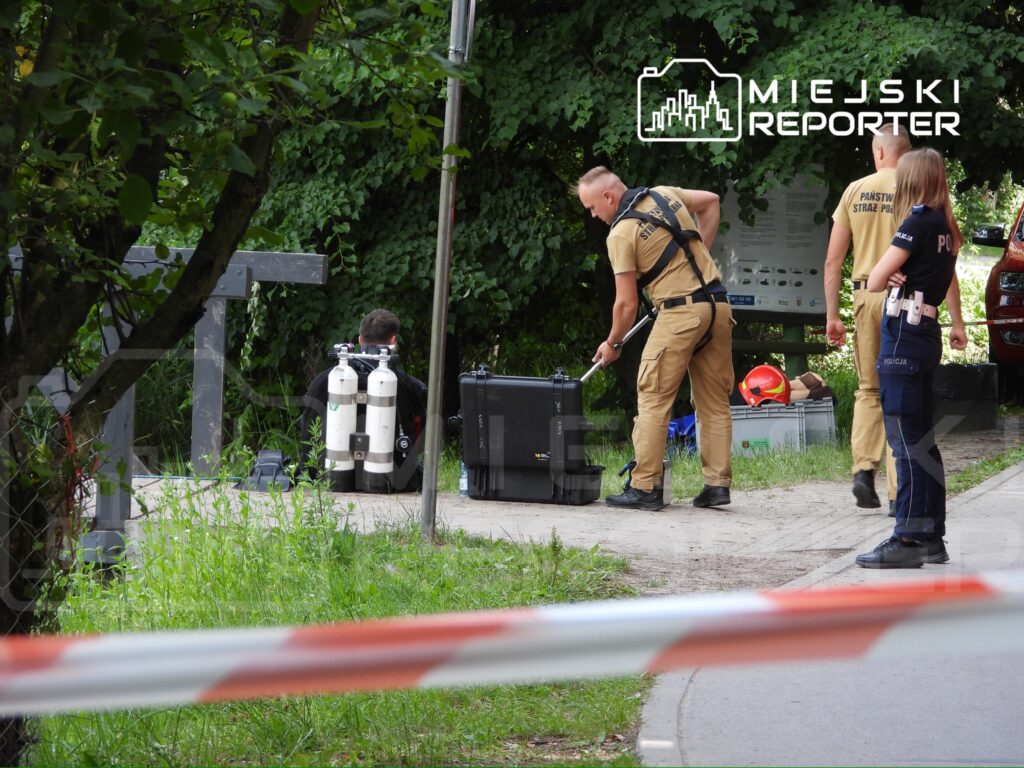 Grupa ratowników w specjalistycznym sprzęcie przygotowuje się do akcji w zarośniętym terenie przy ścieżce.