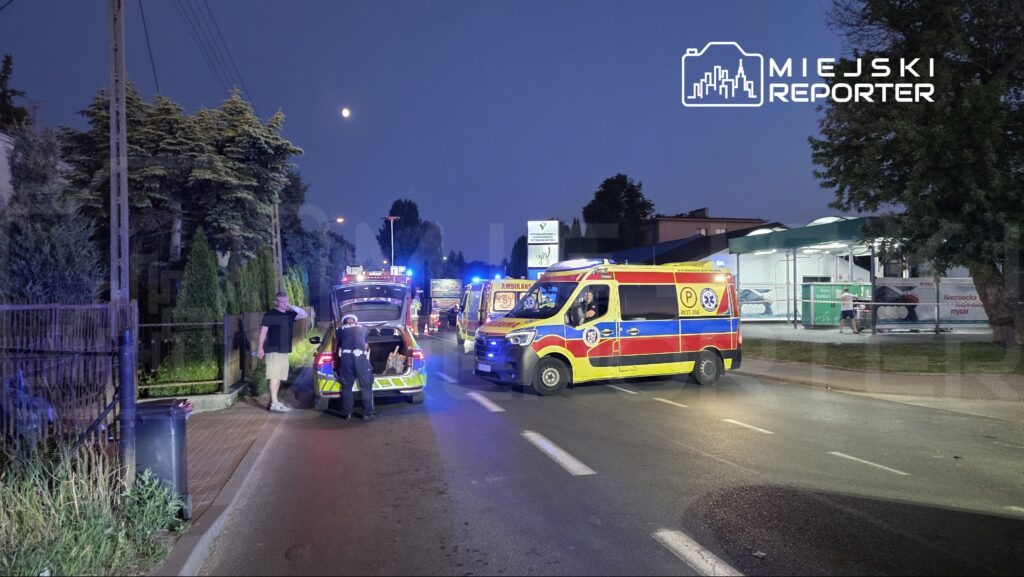 Na drodze zatrzymane są karetki pogotowia oraz radiowóz, a policjant rozmawia z mężczyzną w krótkich spodniach.
