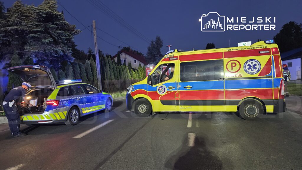 Policjant sprawdzający wyposażenie w bagażniku radiowozu obok karetki pogotowia na ulicy w nocy.