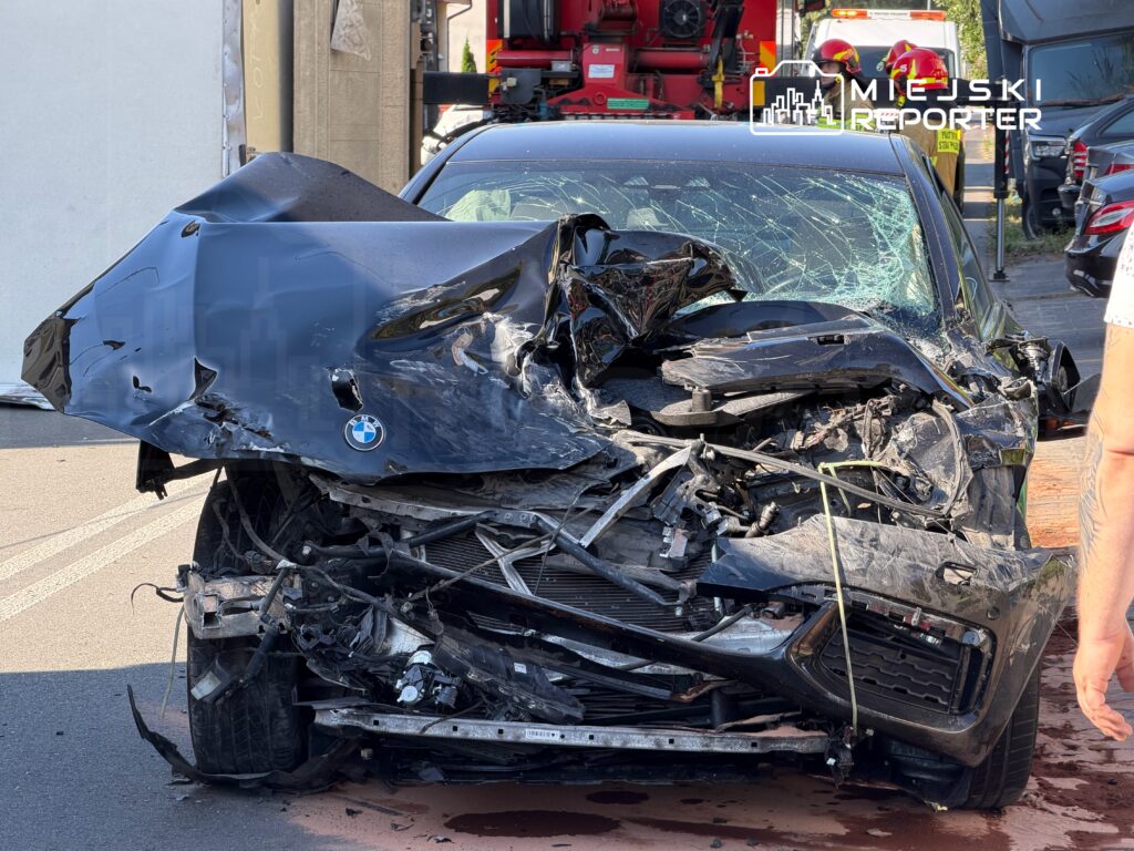 Zniszczony samochód osobowy marki BMW z rozbitym przodem stoi na drodze, obok widać ratowników i sprzęt ratunkowy.