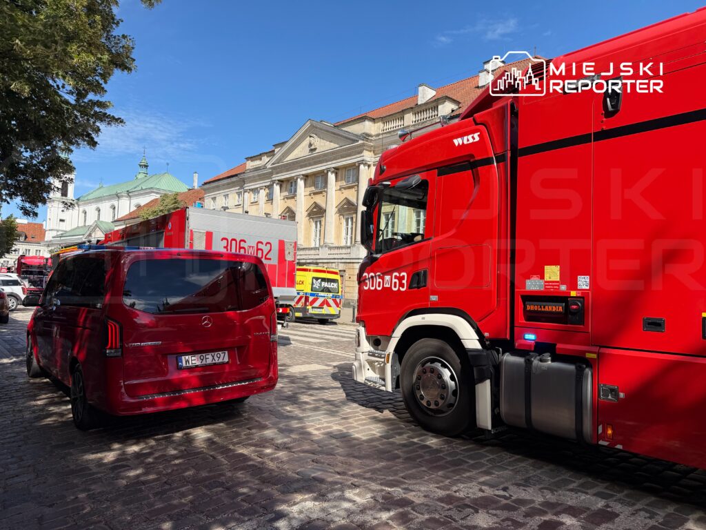 Czerwony samochód osobowy zaparkowany obok dużego czerwonego wozu strażackiego na brukowanej ulicy w mieście.