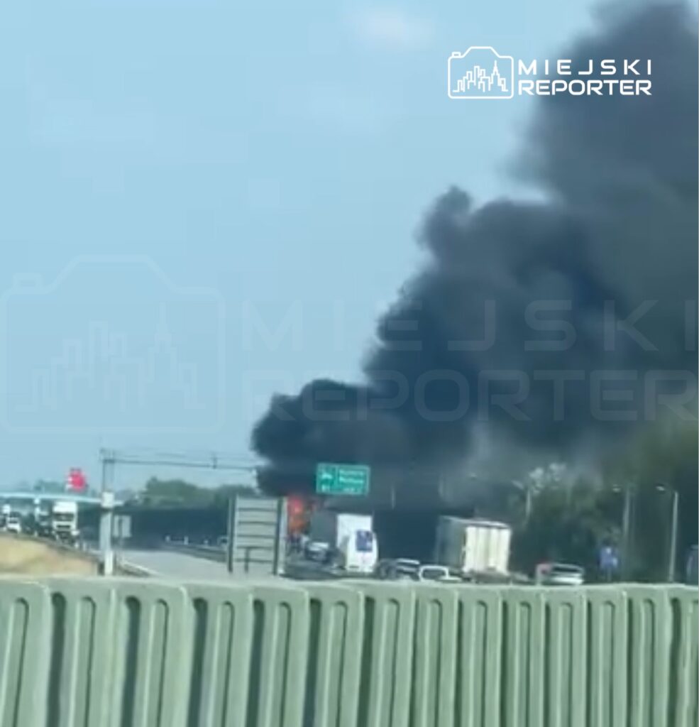 Gęsty czarny dym unoszący się nad autostradą, w tle widoczne samochody stojące w zatorze.
