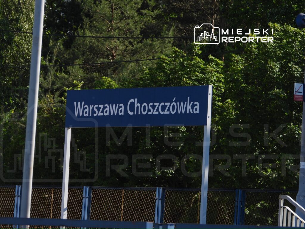 Znak stacji kolejowej "Warszawa Choszczówka" umieszczony na tle zieleni.