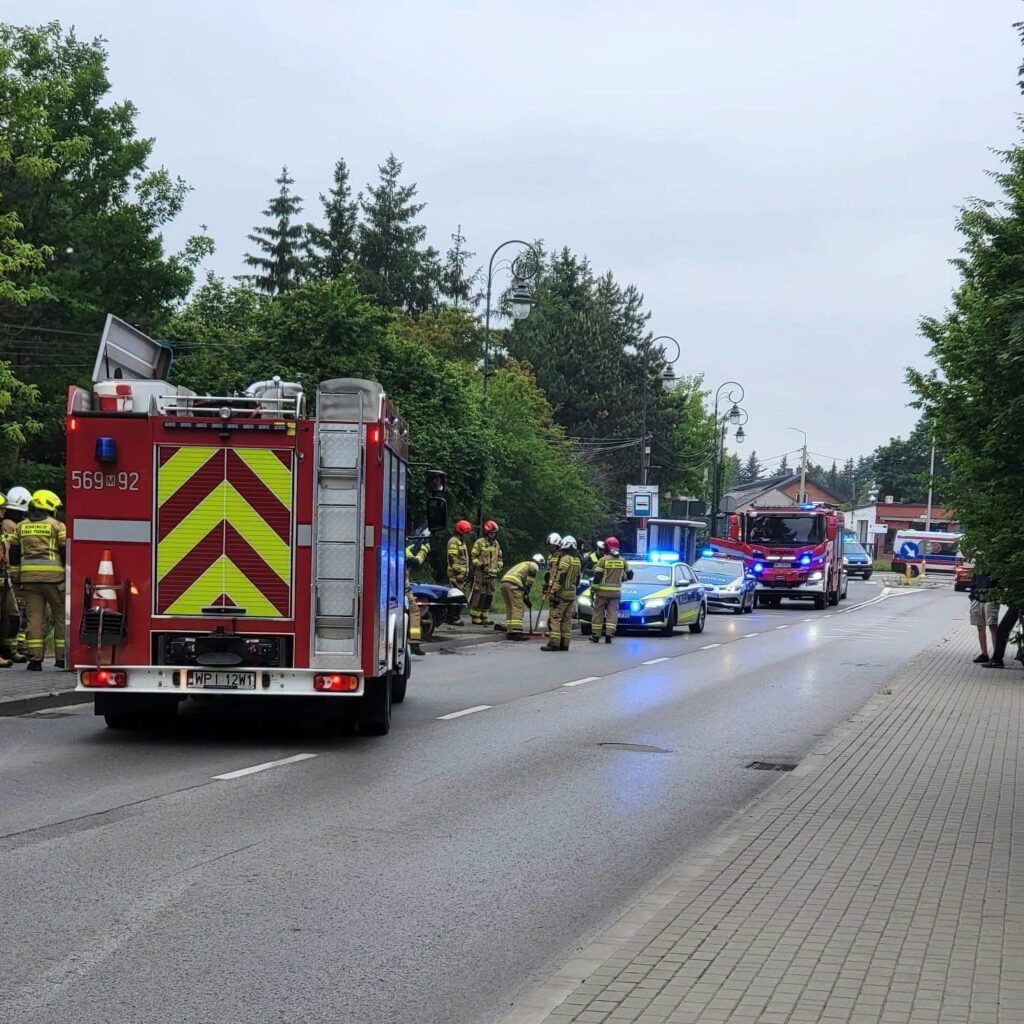 Grupa strażaków i policjantów pracuje przy wypadku drogowym na ulicy, obok zaparkowanej ciężarówki.