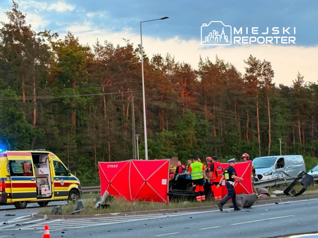 Ratownicy medyczni udzielają pomocy przy wypadku drogowym na trasie, obok czerwonego namiotu i karetki.