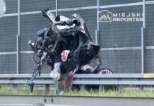 Zniszczony samochód leży na barierze ochronnej, otoczony uszkodzonymi elementami i krwią.