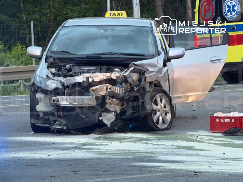 Uszkodzony samochód osobowy z otwartymi drzwiami, stojący na drodze, obok widać ślady płynów eksploatacyjnych.
