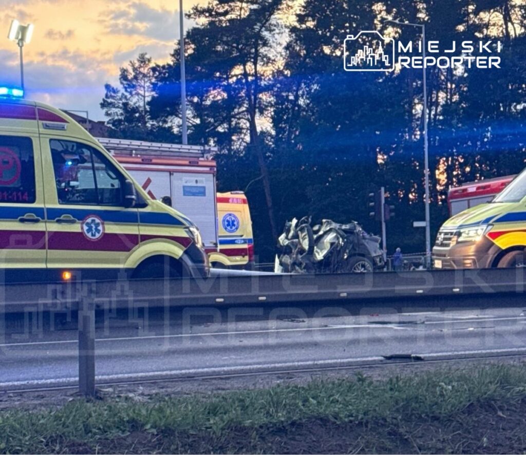 Ambulansy na drodze w pobliżu zniszczonego pojazdu po wypadku, w tle zachmurzone niebo.