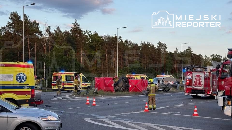 Na drodze widać wypadek, w którym uczestniczą pojazdy ratunkowe oraz strażacy zabezpieczający miejsce zdarzenia.