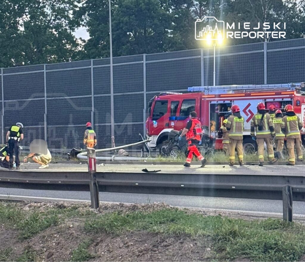 Ratownicy medyczni i strażacy udzielają pomocy poszkodowanemu w wypadku drogowym na poboczu jezdni.