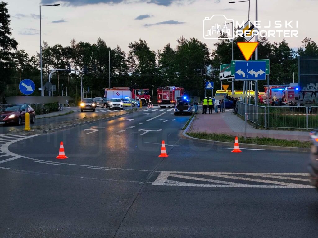 Rondo z włączonymi sygnałami świetlnymi, pojazdy służb ratunkowych oraz ustawione pachołki drogowe.
