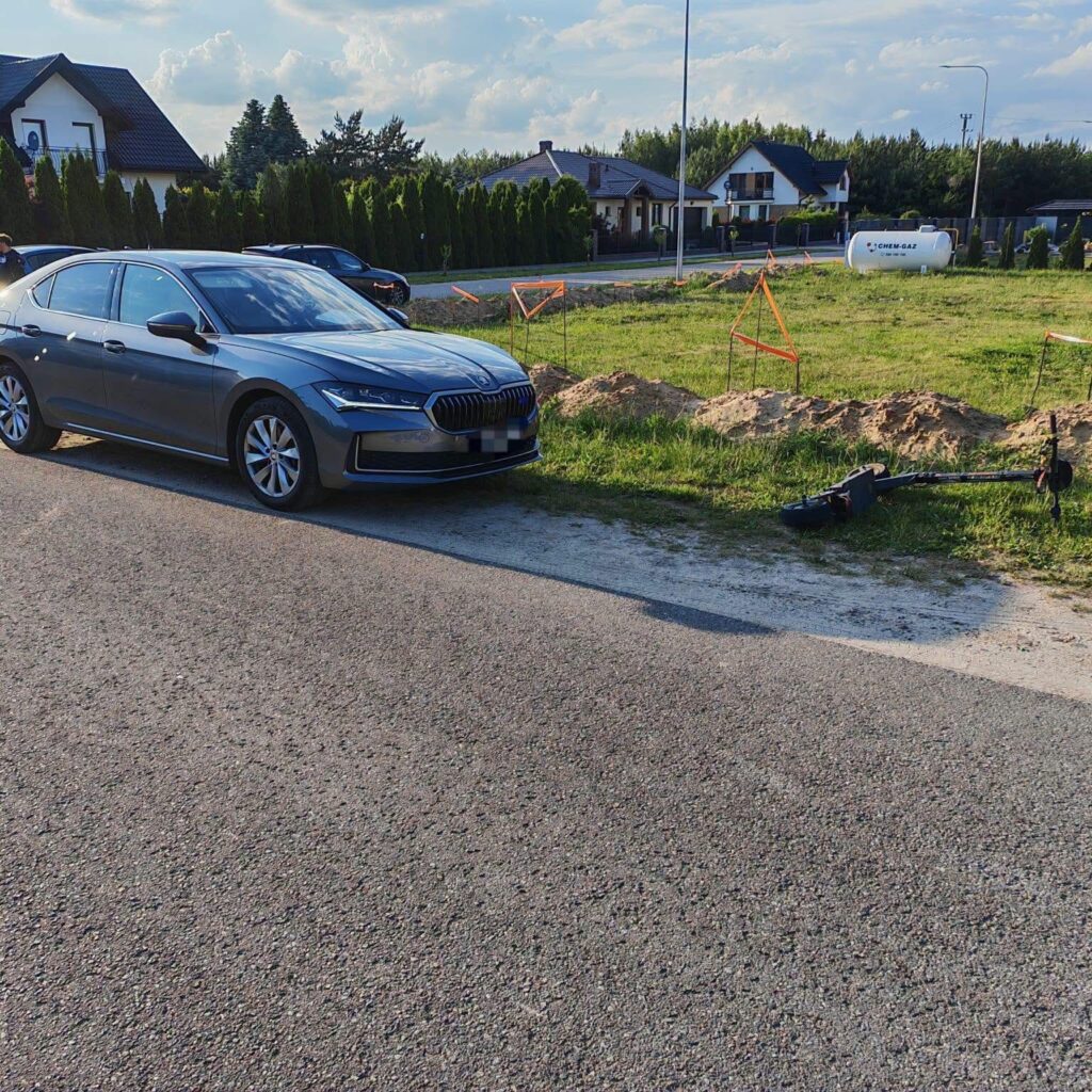 Szary samochód osobowy zaparkowany na poboczu drogi obok terenu budowy z oznaczeniami w postaci pomarańczowych słupków.