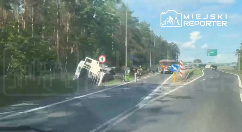Cysterna leży na boku przy drodze, obok niej pracują strażacy i policjanci w lesistym otoczeniu.