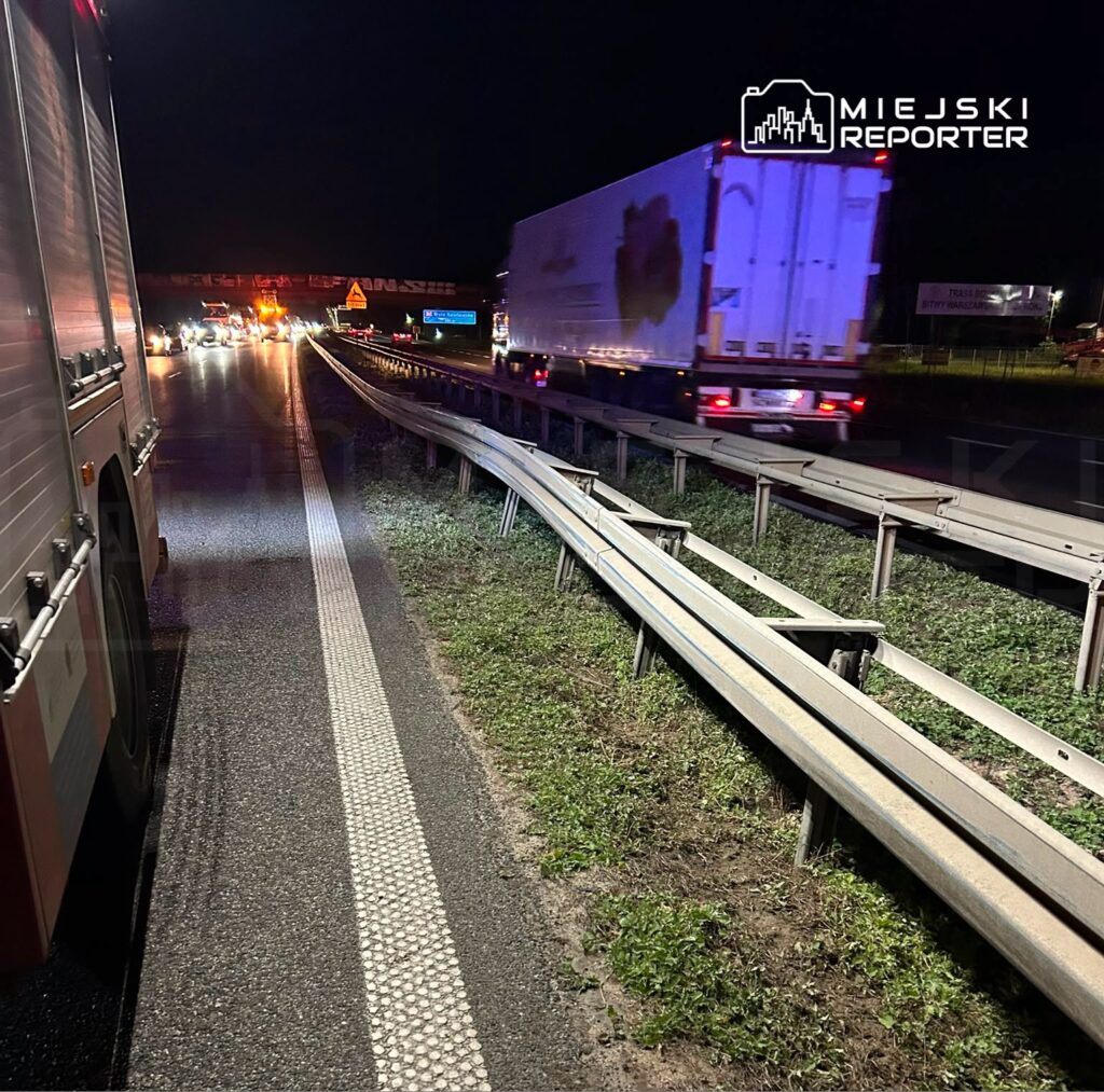 Kierowcy stoją w korku na drodze, obok widać zaparkowany wóz strażacki i migające światła sygnalizacyjne.