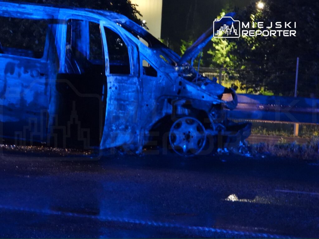Zniszczony pojazd osobowy stoi na poboczu drogi, oświetlony niebieskimi światłami.