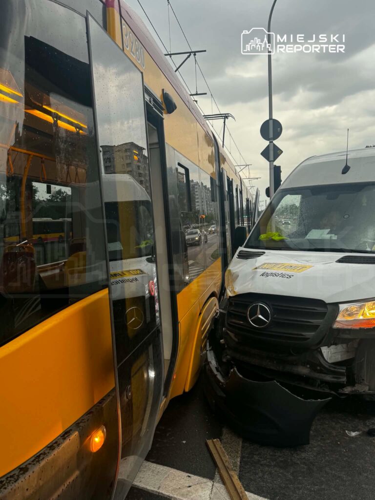 Tramwaj w żółto-czarnym malowaniu zderza się z białym vanem na ruchliwej ulicy w deszczową pogodę.