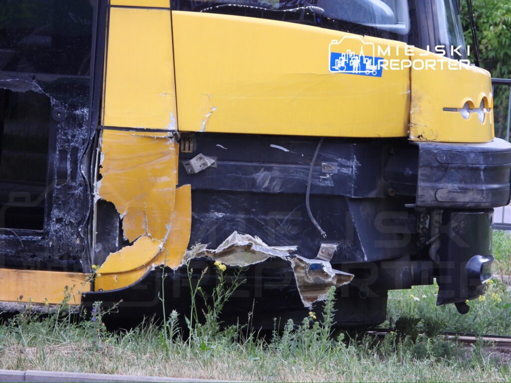 Uszkodzony żółty tramwaj z wyraźnymi wgnieceniami na boku, stojący na trawie obok torów.