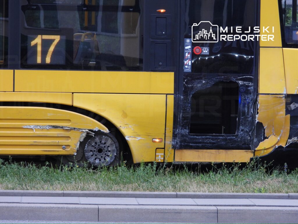 Uszkodzony żółty autobus z widocznymi zarysowaniami na nadwoziu stoi na trawniku obok jezdni.