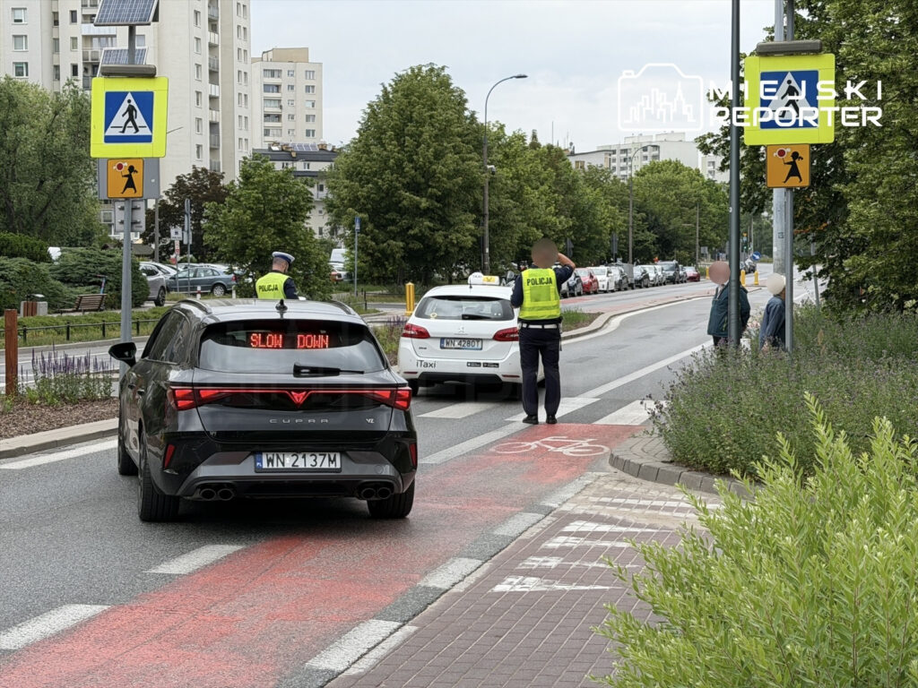 Policjant kierujący ruchem stoi obok samochodu z wyświetlaczem "SLOW DOWN" na ruchliwej ulicy w mieście.