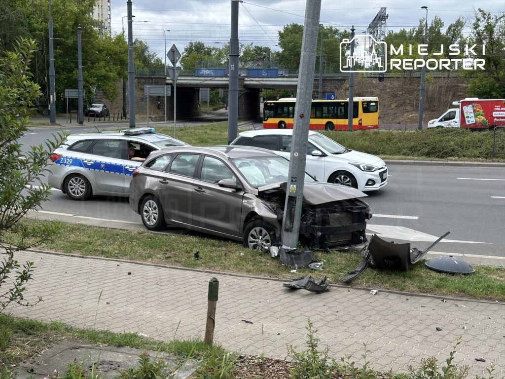 Samochód osobowy uderzył w słup oświetleniowy na skrzyżowaniu, obok stoi radiowóz policyjny.