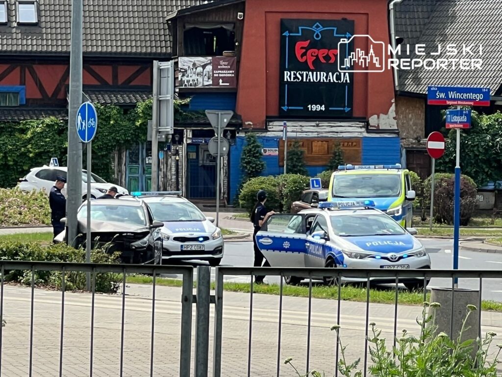 Policjanci prowadzący czynności na miejscu zdarzenia z uszkodzonym samochodem w pobliżu restauracji.